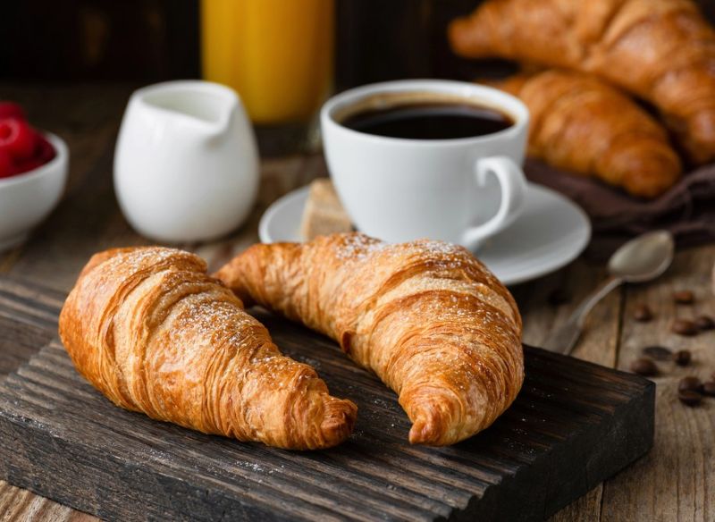 Picture showing a cup of coffee and milk jug with 2 croissants in the foreground, depicting Non-FODMAP dietary triggers for IBS