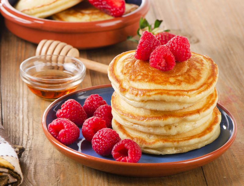A plate showing a pile of low FODMAP Pancakes, topped with raspberries