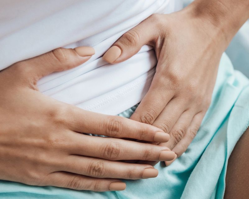Image shows a woman holding her hands across her abdomen in pain. IBS and beyond