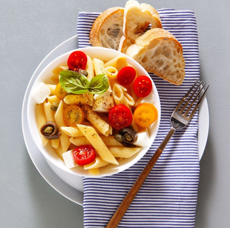 An image showing a dish ofLow FODMAP Chicken & Pasta Salad, sitting on a serving plate with a napkin and fork