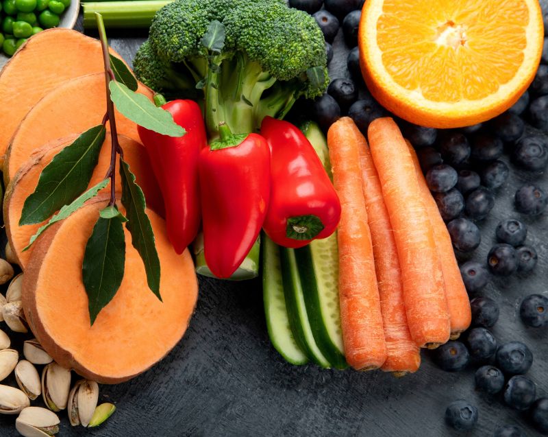 A platter displaying a collection of fruit and veg: squash, brocolli, peppers, carrot, blueberries and orange