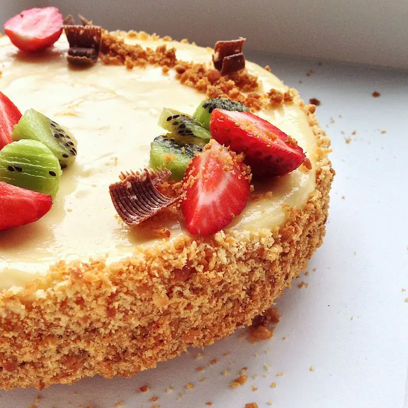 An image showing a Low FODMAP Cheesecake, topped with strawberries, kiwifruit and chocolate shavings