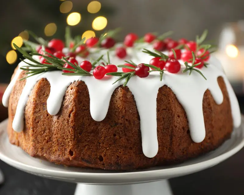 An image showing a Low FODMAP Festive Spiced Cake topped with fresh cranberries and rosemary