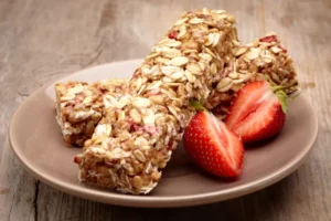 An image showing 2 Low FODMAP Breakfast Bars on a small plate with 2 halves of a strawberry