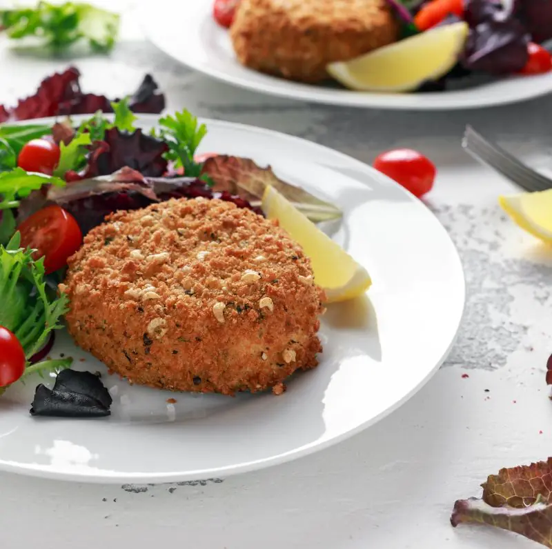 A plate showing low FODMAP Salmon Fishcakes with a small salad and a slice of lemon
